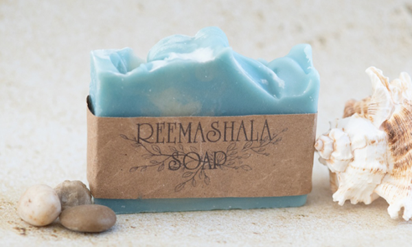 Blue, ocean breeze-scented soap bar flanked by seashells and pebbles.